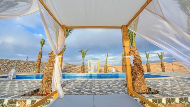 Zona de piscina con suelo a cuadros, palmeras y vistas al desierto.