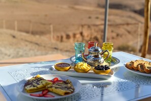 A table with a variety of food items including pancakes, a plate of bread, and several small bowls containing different spreads and fruits. - Pearl Camp Agafay (Marrakech)