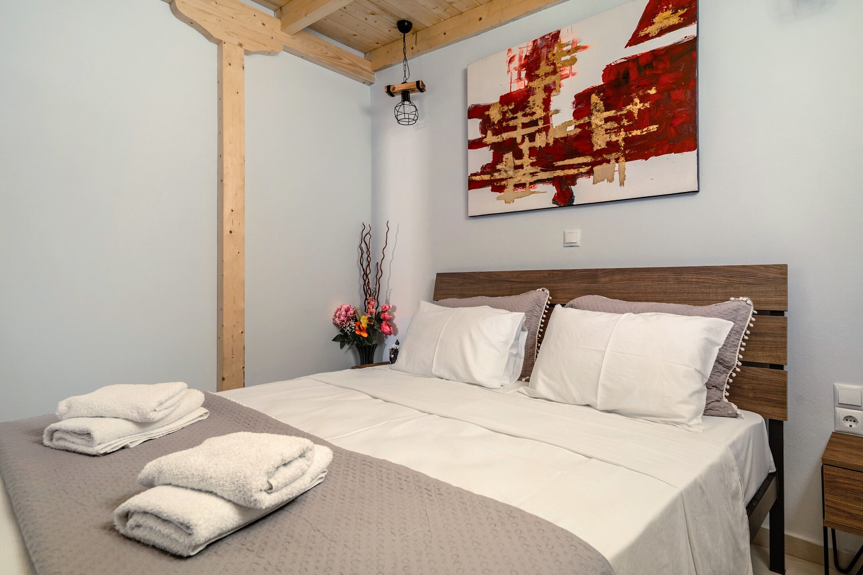 Un lit bien fait, avec du linge de lit blanc, une tête de lit en bois et un tableau abstrait accroché au mur.