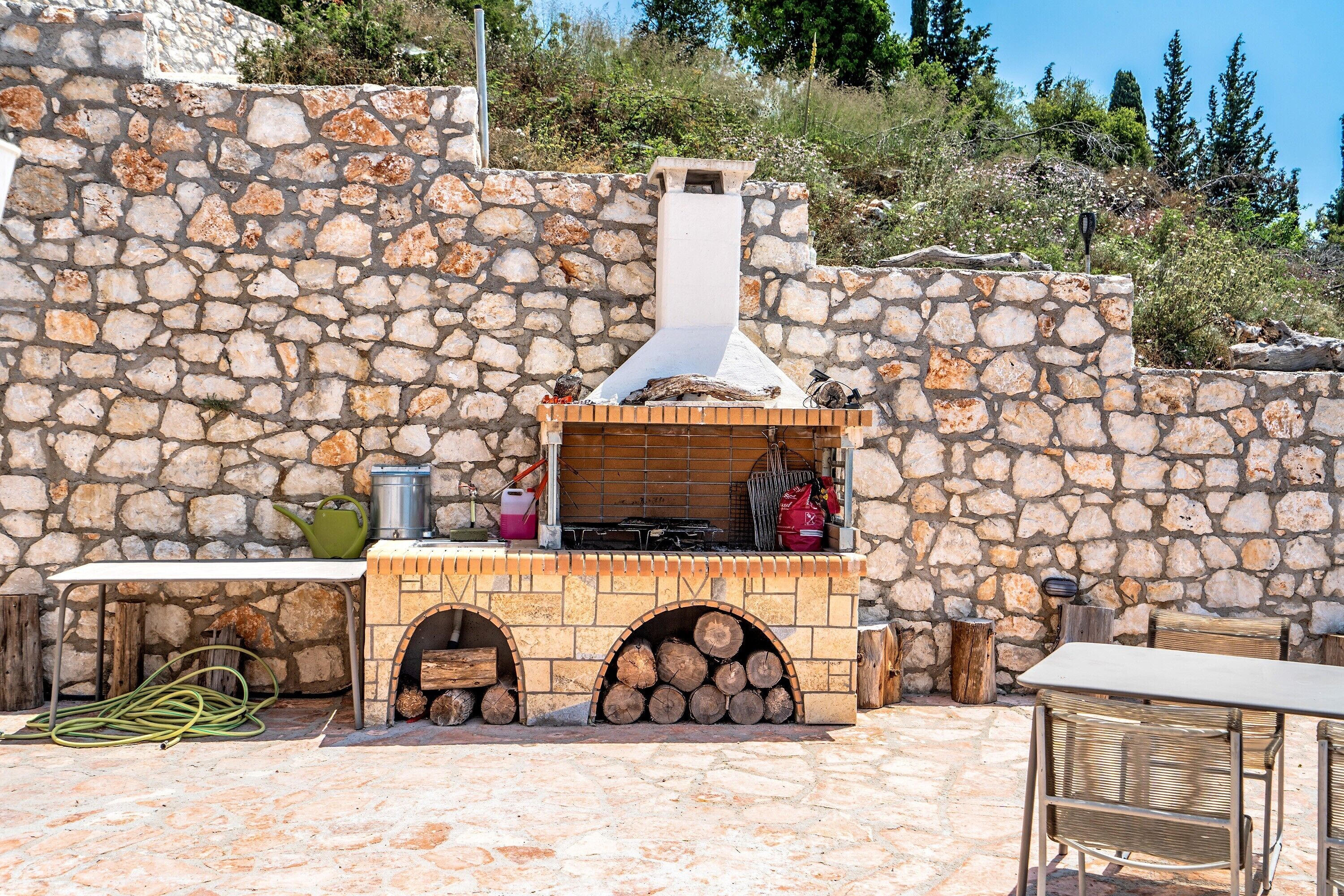 An outdoor stone wall with a built-in wood stove and a table with chairs.