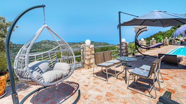 A patio with a hanging chair, a table, chairs, and a pool. - Apartment 'Ventus Artemis' with Sea View, Wi-Fi and Air Conditioning (Lefkada)