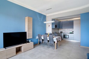A modern living room with a flat-screen TV, dining table, chairs, and a kitchen area with cabinets and appliances. - Apartment 'Glamuor 1' with Private Terrace, Wi-Fi and Air Conditioning (Sanremo)