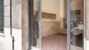 Ingresso di un edificio con porta in vetro, pavimento in marmo e una scalinata interna.