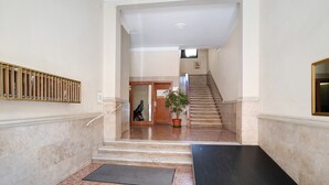 Un corridoio con pavimento in marmo, una scala, una pianta in vaso e una telecamera di sicurezza.