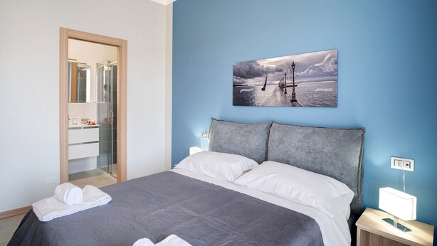Una camera da letto con un letto, un comodino, una lampada a parete, un quadro e uno specchio.