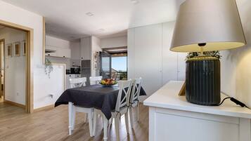 A modern kitchen with white cabinets, a dining area with a table set for four, and a large lamp on a white console table.
