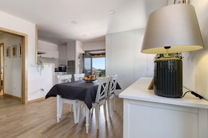 A modern kitchen with white cabinets, a dining area with a table set for four, and a large lamp on a white console table. - Holiday Home 'Da Lage' with Sea View, Wi-Fi and Air Conditioning (Castelo do Neiva)