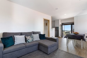A grey sectional sofa with pillows, a dining table with chairs, and a view to the outside. - Holiday Home 'Da Lage' with Sea View, Wi-Fi and Air Conditioning (Castelo do Neiva)