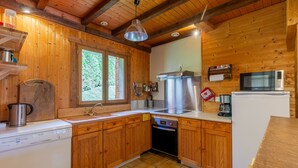 A wooden cabin kitchen with a dishwasher, stove, microwave, and a large window. - Chalet "L'Oréade" with Mountain Views, Private Terrace and Wi-Fi (Manigod)