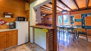 A kitchen with wooden cabinets, a refrigerator, a microwave, and a dining area with chairs and a table. - Chalet "L'Oréade" with Mountain Views, Private Terrace and Wi-Fi (Manigod)
