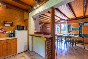 Una cocina con armarios de madera, un refrigerador, un microondas y un comedor con sillas y una mesa.