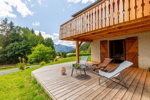 Une terrasse en bois avec des meubles d’extérieur, un balcon doté de rampes en bois et un paysage montagneux en toile de fond.