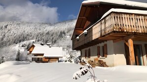 A snow-covered mountain with wooden buildings, including a chalet with a balcony. - Chalet "L'Oréade" with Mountain Views, Private Terrace and Wi-Fi (Manigod)