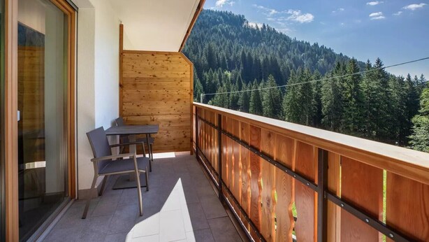 Ein Balkon mit Tisch und Stühlen, Holzwände und Blick auf einen bewaldeten Berg.