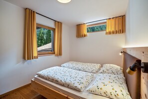 Une chambre avec un lit en bois, deux fenêtres avec des rideaux et une vue sur la verdure à l’extérieur.