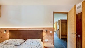 Une chambre à coucher avec une tête de lit en bois, un lit recouvert d’une literie à motifs floraux, une table de chevet et une armoire en bois.