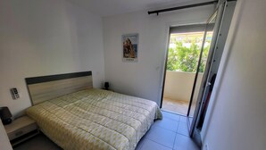 A bedroom with a bed, a nightstand, a wall-mounted phone, and a door leading to a balcony.