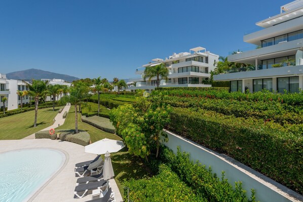 A modern resort with a swimming pool, lounge chairs, and a well-maintained garden.