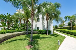 Un jardin bien entretenu, agrémenté de palmiers, un bâtiment blanc et un chemin pavé.