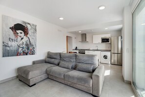 Een moderne woonkamer met een grijze modulaire bank, een keuken met roestvrijstalen apparatuur en een groot abstract schilderij aan de muur.