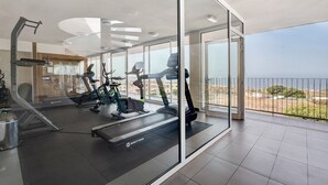 A modern gym with treadmills, stationary bikes, and a rowing machine, featuring large windows and a balcony with a view of the sea. - Vacation Home 'Suite Mirador Del Galeón' with Sea View, Wi-Fi and Air Conditioning (Adeje)