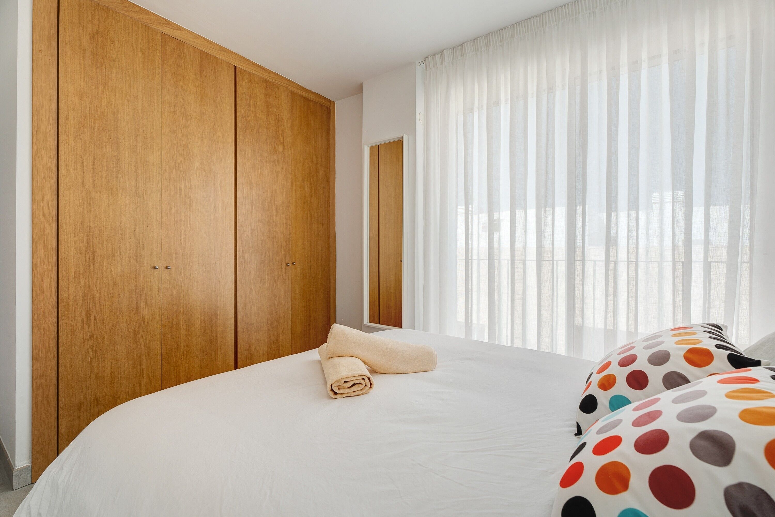 A bedroom with a large bed, wooden wardrobe, and a window with sheer curtains.