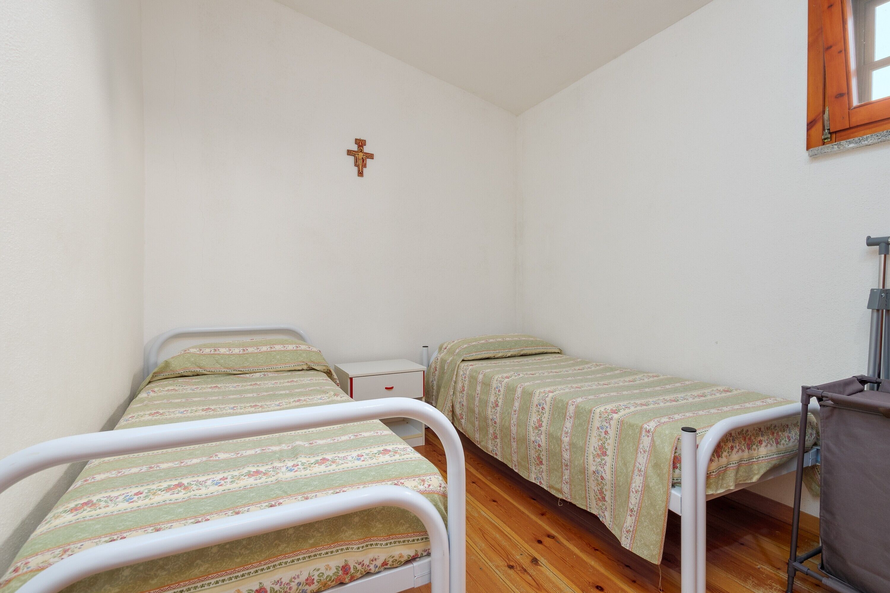 Ein kleines, sauberes Zimmer mit zwei Einzelbetten, Holzboden, weißer Wand und einem Fenster mit Holzrahmen.