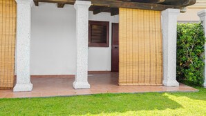 Un edificio con un vestíbulo cubierto, columnas, una puerta con ventanal y un seto verde.