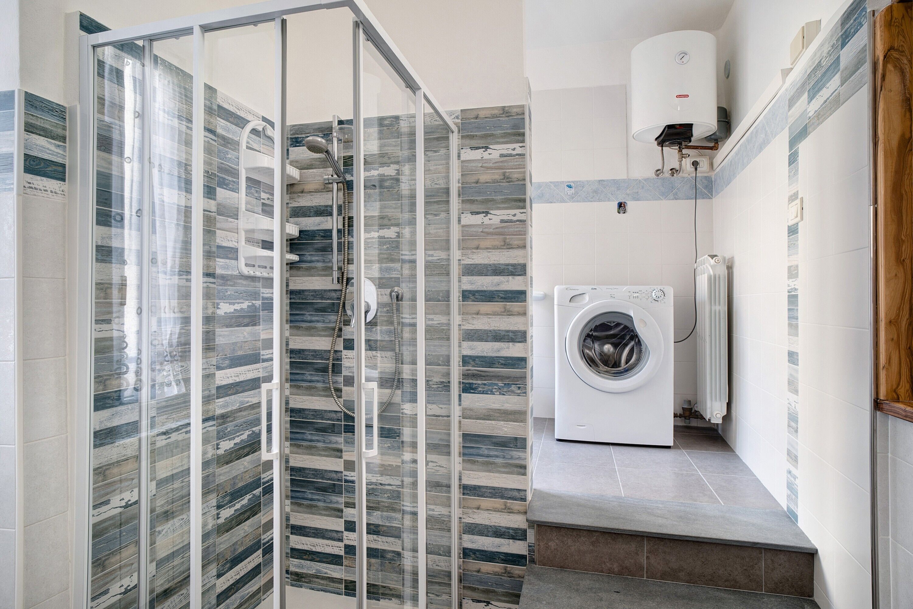 Un baño moderno con cabina de ducha de vidrio, lavadora integrada y salpicadero de azulejos.