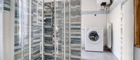 Un baño moderno con cabina de ducha de vidrio, lavadora integrada y salpicadero de azulejos.