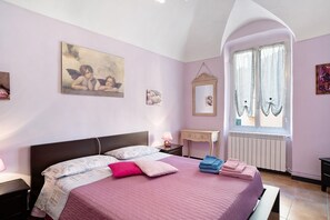Un dormitorio con cama, mesita de noche, cómoda, ventana con cortinas y decoración en la pared.