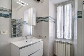 Un baño con lavamanos blanco, espejo y ventana con cortinas.
