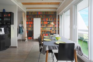 Comedor con una mesa preparada para cuatro, una estantería al fondo y vistas al exterior a través de amplias ventanas.