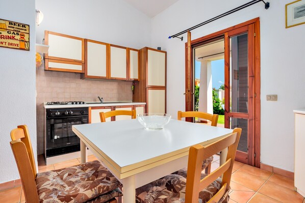 A compact kitchen with wooden cabinets, a gas stove, and a dining table with chairs.