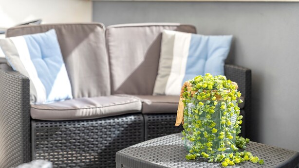 A wicker sofa with grey cushions and a glass vase with yellow flowers on a grey table. - Apartment 'Isola Di Giava Holiday' with Private Terrace, Wi-Fi & Air Conditioning (Sorso)