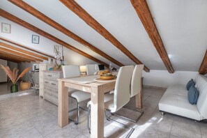 Un espace repas avec une table et des chaises en bois, un canapé et, au fond, une cuisine.