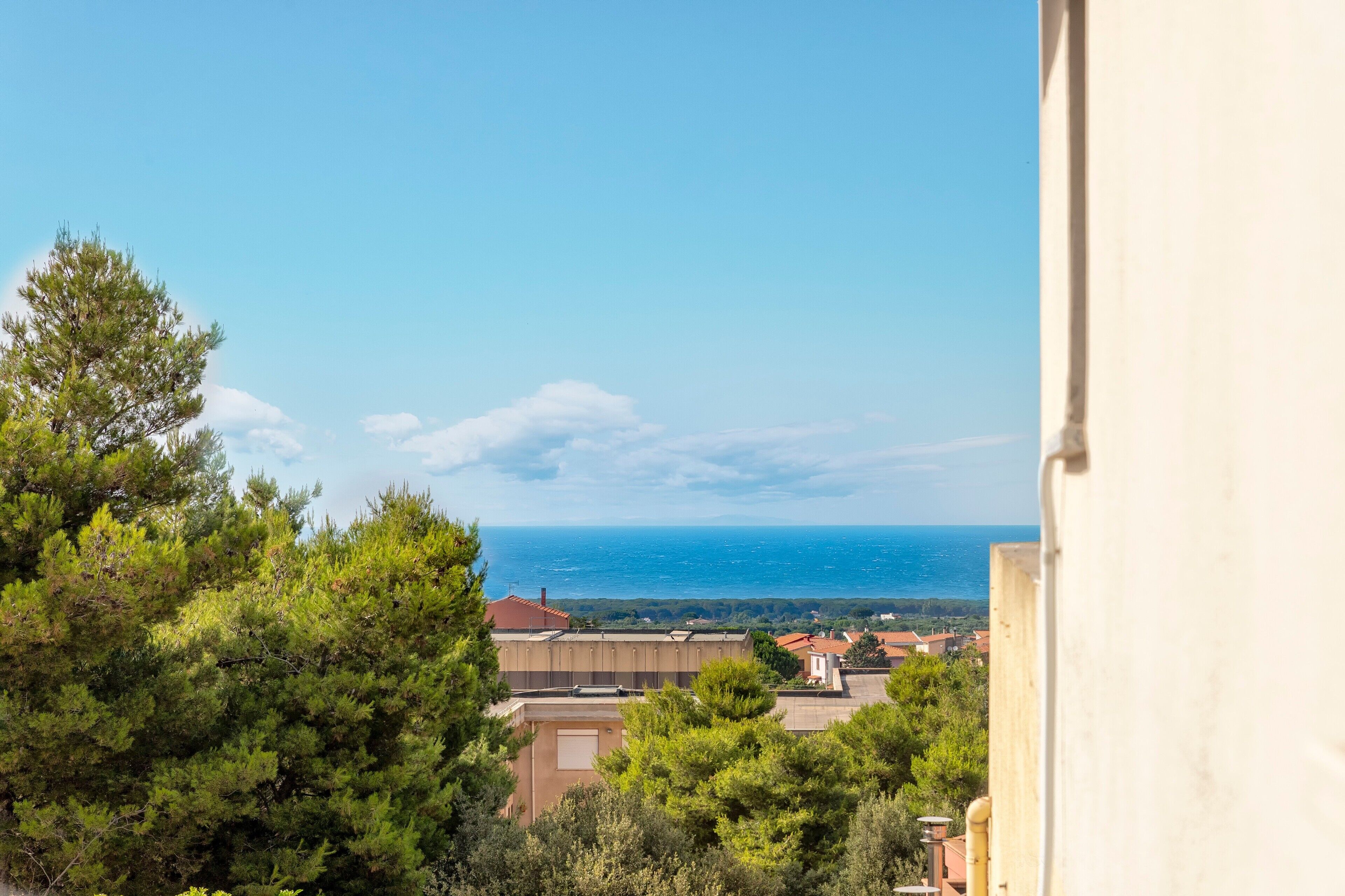 Vista costiera con edifici, alberi e il mare.