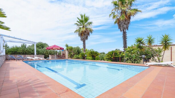 A swimming pool with tiled edges, surrounded by palm trees and a pergola. - Villa 'Venza with Pool' with Private Pool, Private Garden and Wi-Fi (Ostuni)