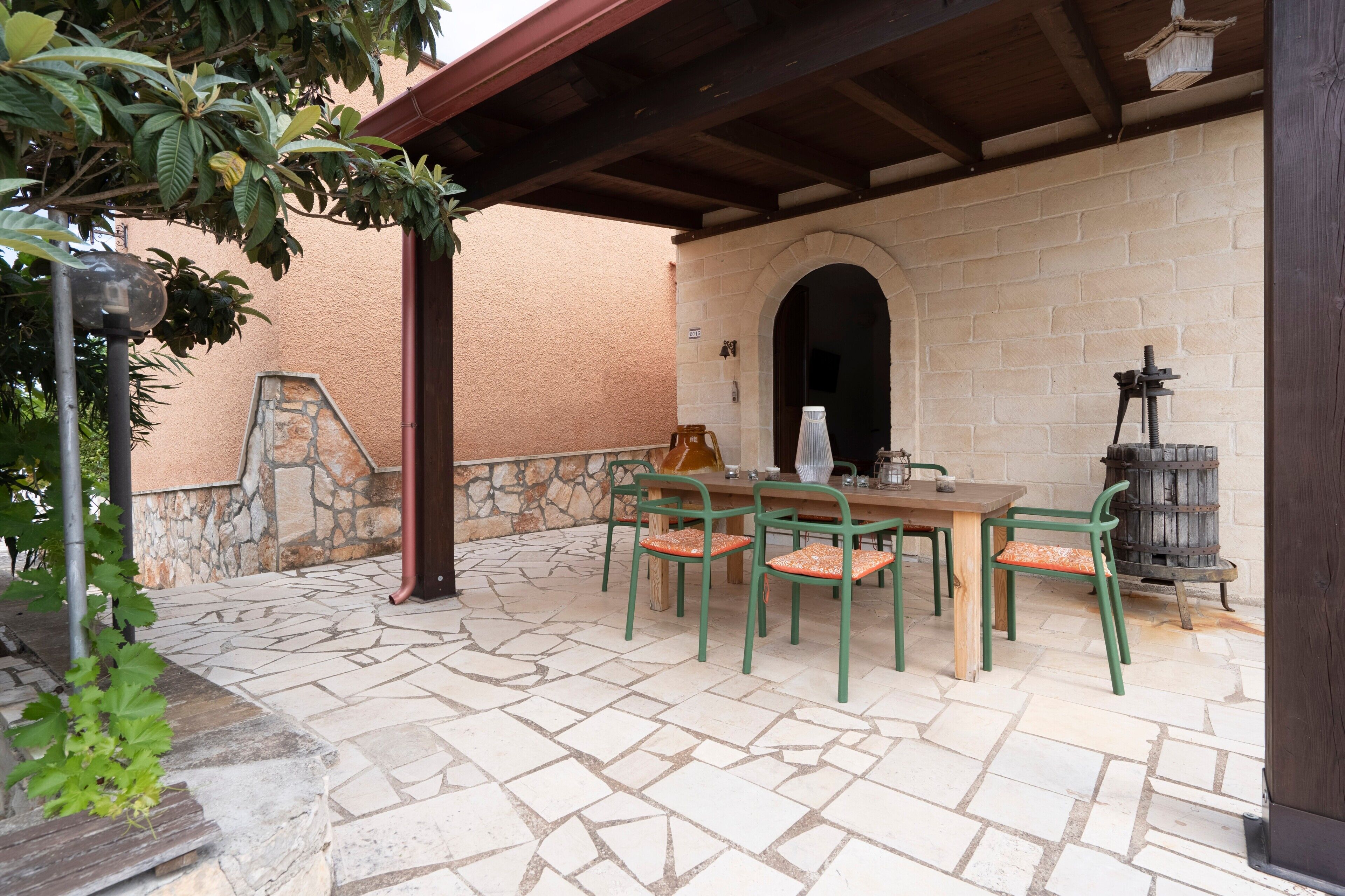 An outdoor patio with stone flooring, a wooden table, green chairs, and a brick wall.