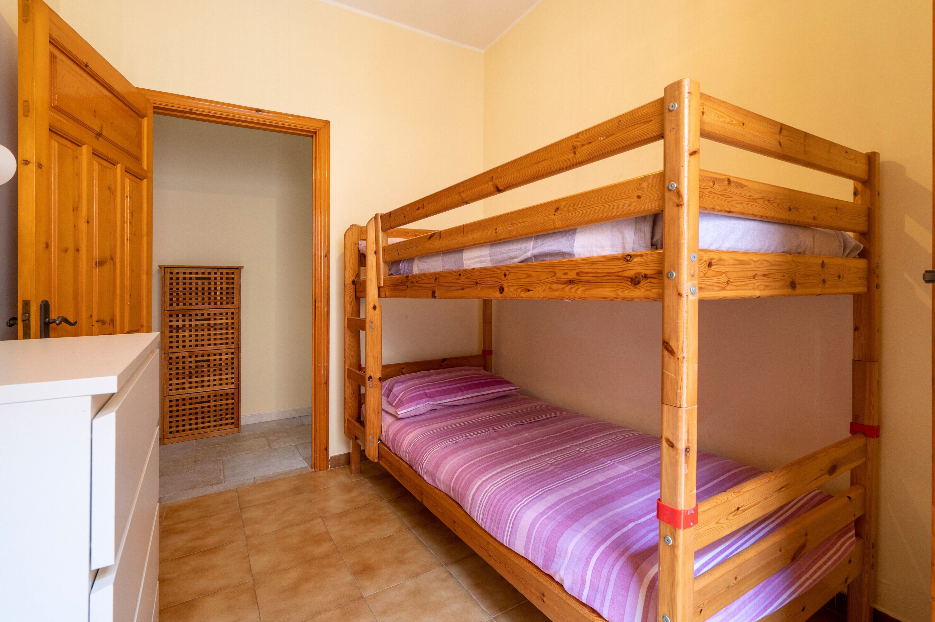 Un lit superposé avec une structure en bois, un bureau blanc et une porte en bois.