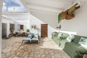A stone-floored patio with a green-striped sofa, a table with chairs, and a door. - Holiday Home "Casa Rural Atalaya-Coy" with Mountain Views, Private Terrace and Garden (Coy)