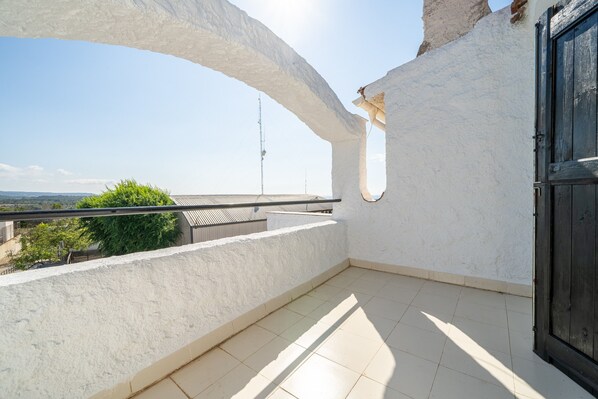 A balcony with a white wall, a black door, and a view of a distant tower.