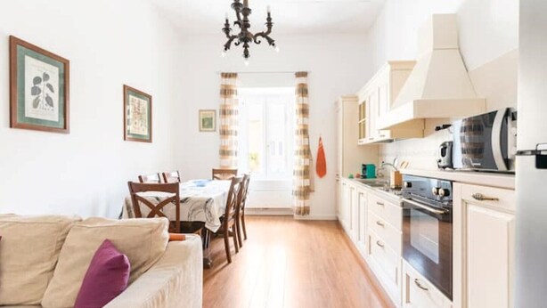 Ett kompakt bostadsutrymme med en matplats, ett litet kök och en soffa med en kudde.