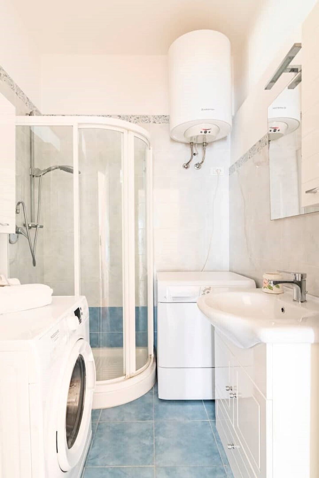 Une salle de bain moderne dotée d’une douche à parois de verre, d’un lave-linge encastré et d’un lavabo avec un miroir au-dessus.