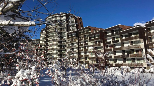 Un immeuble résidentiel à plusieurs étages, dot é de balcons, entouré d’arbres et d’arbustes couverts de neige.