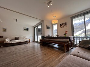 Ein geräumiges Wohnzimmer mit Holzboden, einer Couch, einer Bank und einem Tisch mit Blick auf Berge durch große Fenster.
