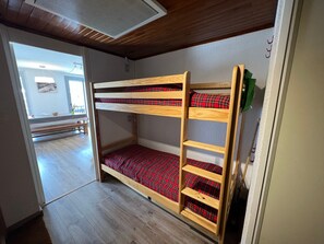 Un lit superposé avec une literie à carreaux rouges, dans une pièce au plancher en bois et au plafond en pente.