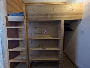 A wooden bunk bed with a blue mattress at the top and a lower bunk with a ladder.