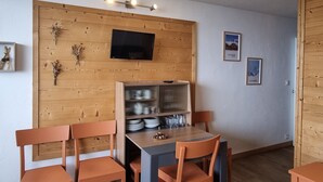 Un coin repas avec un mur en bois, un téléviseur et une étagère où sont rangés de la vaisselle.