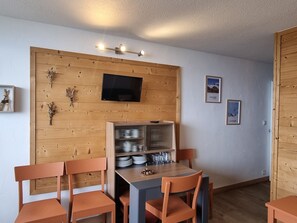 A dining area with a wooden wall, a television, and a shelf with dishes.